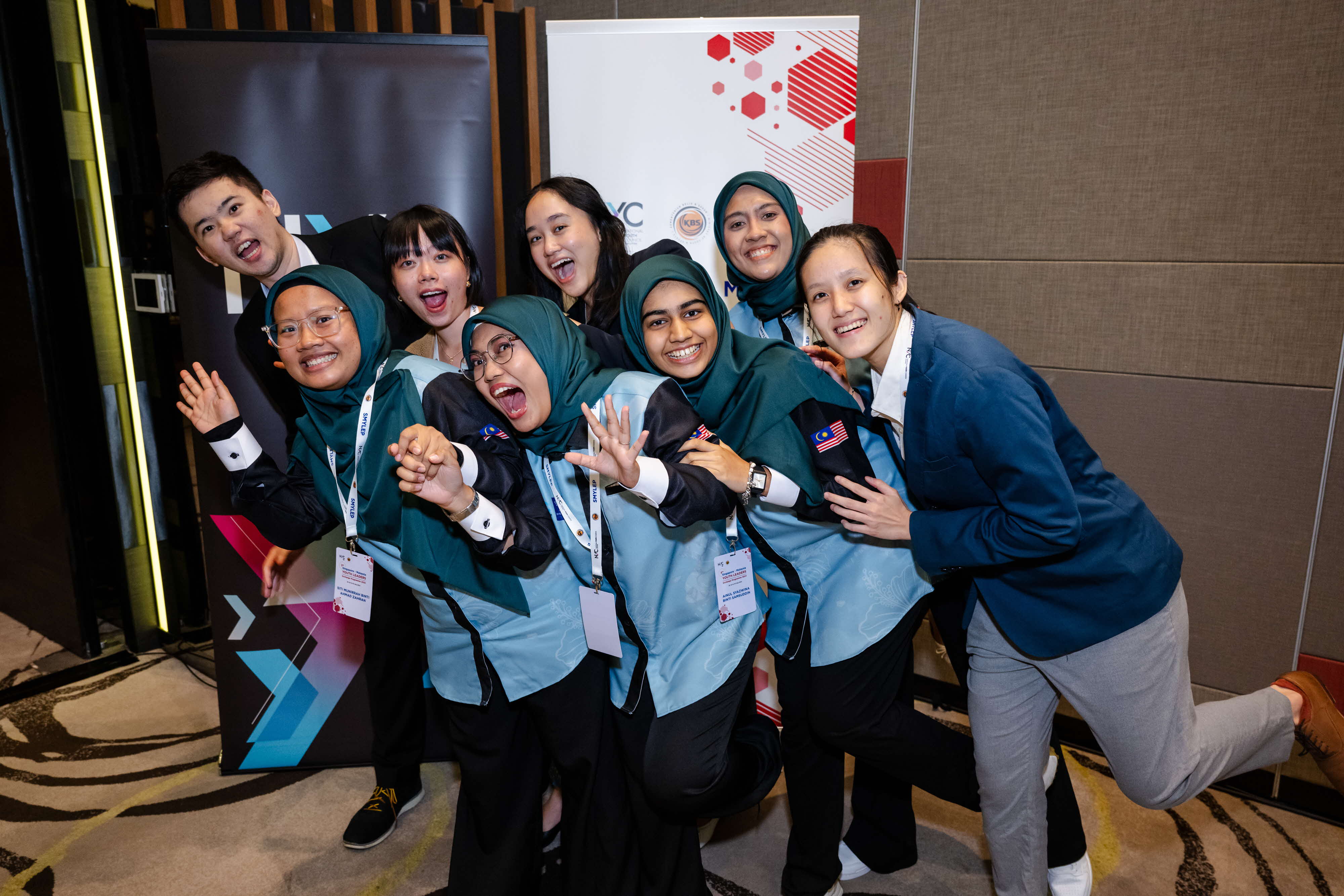 Group of people leaning on each other, posing for a photo in front of a National Youth Council standee.
